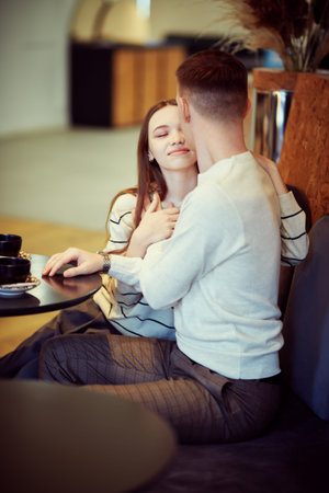 Pretty girl and handsome young man sit close to each other at a table in a cozy cafe and kissing....