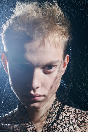 Close up portrait of a young man in black turtleneck with black mesh fabric on his head looking...