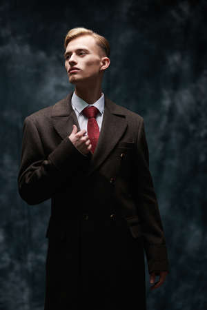 Men's beauty, fashion. Respectable handsome young man in elegant coat and classic suit stands on a dark background.の写真素材