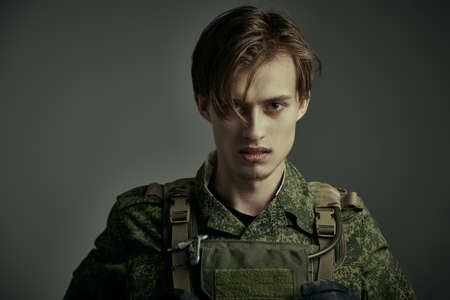Portrait of a furious, courageous soldier in camouflage looking resolutely into the camera. War, battle with the enemy. Studio portrait on a dark gray background.の写真素材