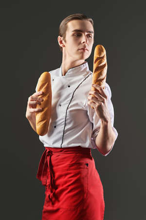 Studio portrait of a professional male chef holding two fresh baguettes. Food and meals.の写真素材