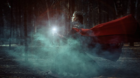 Sideview shot of a majestic, beautiful noble woman in a dark forest with a magic sword in her hands. Scandinavian mythology. Ancient legends.の写真素材