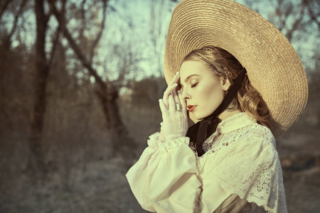 Portrait of a pretty romantic girl in a white dress and a straw hat in an old autumn park. Victorian...