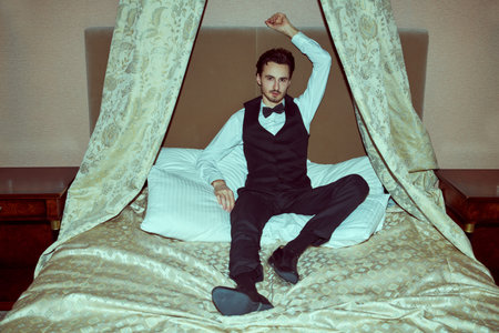 Glamor lifestyle. An attractive brunet man in an elegant evening suit lies on a bed in a luxury...