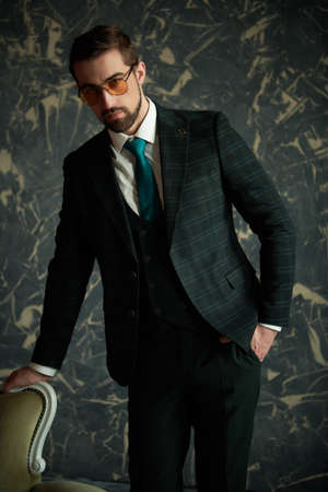 Serious and respectable man in elegant classic three-piece suit and sunglasses poses in a vintage apartment. Men's beauty, fashion. Luxury style.の写真素材