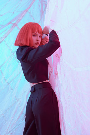 Gorgeous female fashion model with bright makeup and red shoulder-length hair poses in stylish black...