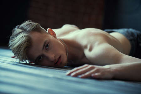 Art portrait of a young man with a thin naked torso lying on the floor with his face expressing sadness and suffering. Emotions, inner world, psychology.の写真素材