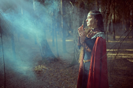 Ancient legends. A beautiful medieval queen stands in a dense forest shrouded in fog and looks at...