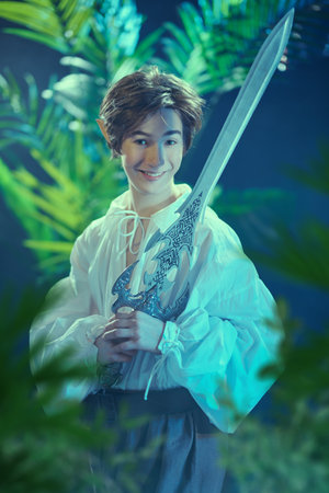 Cheerful young fairy elf stands in a forest with a sword in his hands and joyfully smiles. Fantasy. Fairy tale, magic.の写真素材