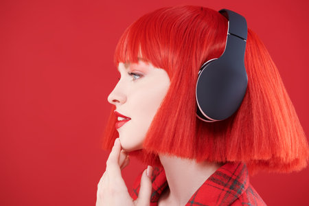 Sideview shot of a stylish girl with bright red lips and red hair wearing red checkered jacket and...