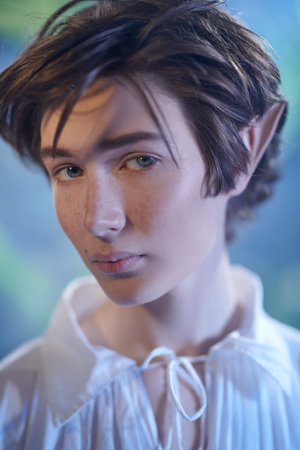 Fairy tale, magic. Portrait of a handsome fairy elf boy in a forest looking pensively at the camera....