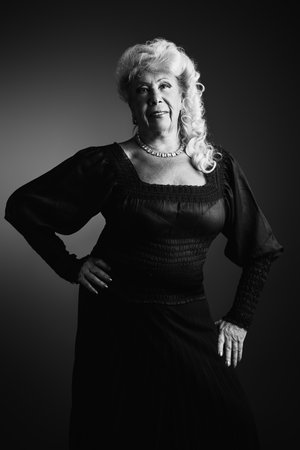 Black and white portrait of a beautiful elderly woman of 80 years old in a black evening dress and evening make-up and hairstyle. Elderly age. Fashion for the elderly. Studio portrait.の写真素材
