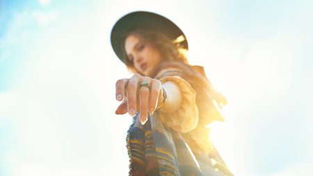 A modern girl in boho style clothes and hat reaches out her hand to the camera in the background of...