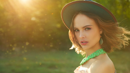 An attractive girl in boho style clothes and accessories standing in the countryside in warm rays of the sun. Summer vacation. Bohemian, modern hippie style. Copy space.の写真素材