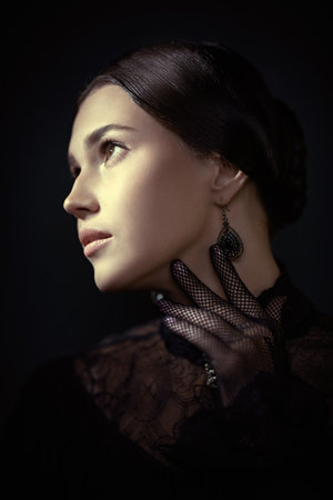 A classic portrait of a 19th century aristocratic girl with dark hair and a strict black dress. Black background. Historical portrait.の写真素材