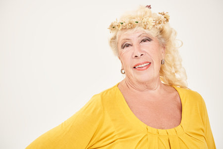 Studio portrait of a romantic senior woman in her 80s wearing a flower wreath smiling at the camera....