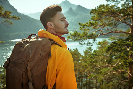 A man tourist hiker climber with a backpack behind his back stands against the backdrop of a...