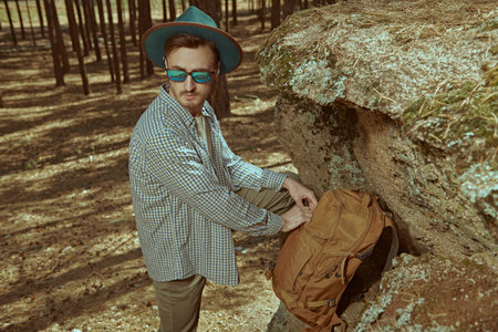Adventures, summer tourism. Portrait of a handsome young man backpacker standing in a pine forest...