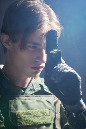 An Army soldier in Protective Combat Uniform holds a gun in front of his face being absorbed in his...