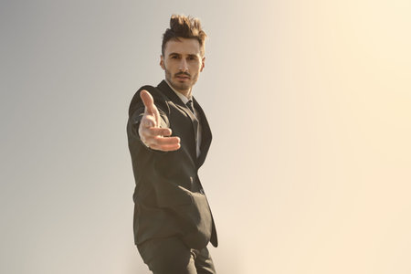 A man in a business suit stands on the top on the background of the sunny sky extending a helping...