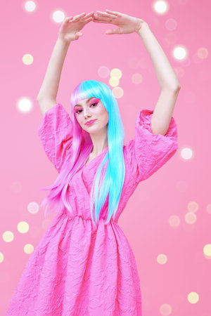 Cute girl with bright makeup and in colored violet-blue wig posing in stylish pink dress. Pink...