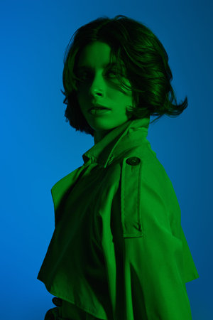Fashion shot. Beautiful brunette girl model posing at the studio in a raincoat in green light on a...