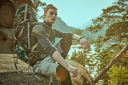 A tourist mountaineer with a backpack on his back rests on a mountain. Mountain hiking, active lifestyle. Extreme sport.の写真素材
