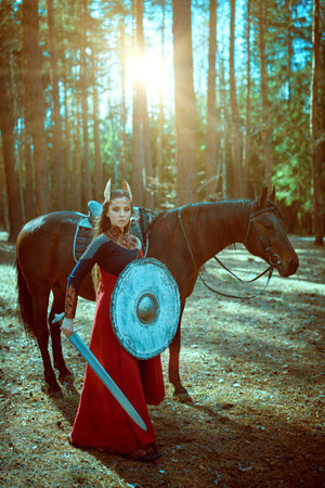 Portrait of a courageous woman warrior valkyrie with a sword and shield standing on alert in the...