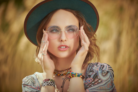 A beautiful romantic girl in boho style clothes and accessories poses in a field near the reeds....