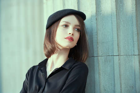 A romantic brunette girl with a bob haircut, dressed in a black beret and a black blouse, stands in the center of the city and looks melancholy to the side. Style and fashion. Makeup and haircut.の写真素材