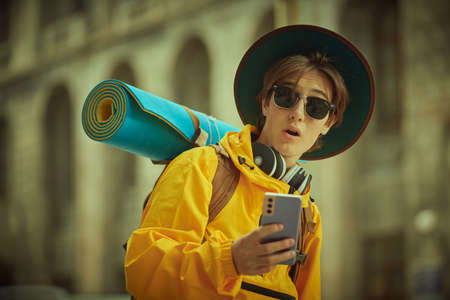 A young tourist, a teenager boy with a backpack, is sightseeing the city with big surprise holding a smartphone in his hand. Holidays, travel. Active, educational lifestyle.の写真素材