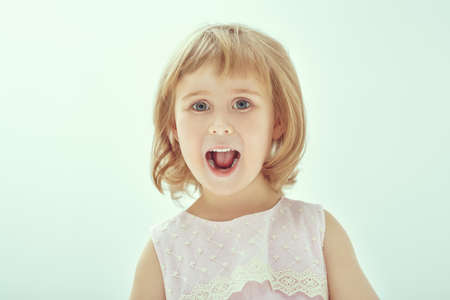 Portrait of a cute little girl looking with surprise at the camera and screaming for joy. Studio portrait on a white background. Children and emotions.の写真素材