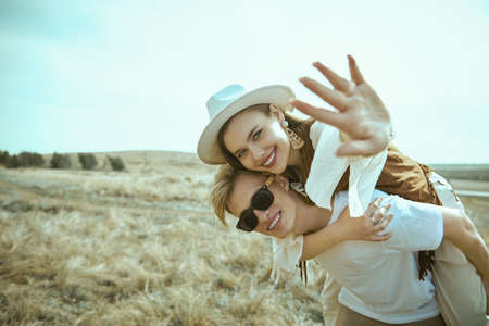 Summer vacation and travel. Handsome guy carries a pretty smiling girl on his back. Beautiful landscape and blue sky background. Love, summer, freedom. Happy loving couple.の写真素材