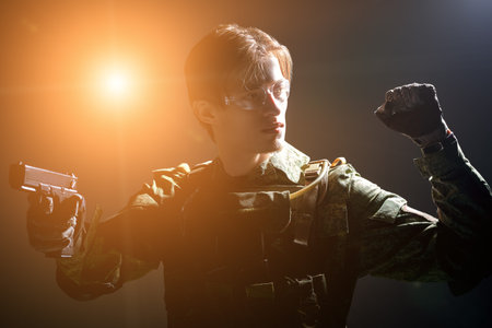 Army soldier in camouflage fights with a gun. A beam of bright light illuminates him from behind....