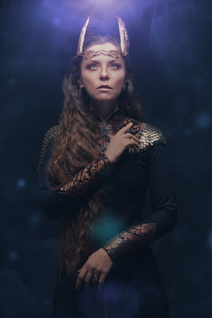 Portrait of a beautiful valkyrie woman standing on a black background looking up at the bright light. Scandinavian mythology. Fantasy.の写真素材