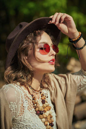A romantic brunette girl in boho style clothes and accessories stands in the park on a sunny day. Boho and hippie style. Summer, vacation.の写真素材