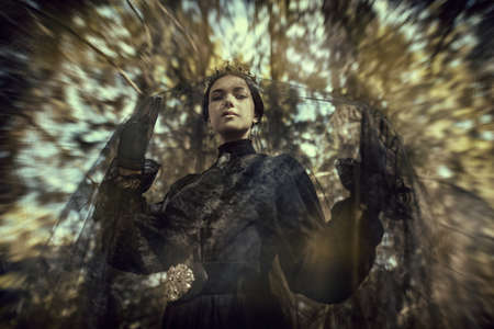 Beautiful Black Queen. A beautiful young woman in a mourning veil, black dress and a crown stands in a dark forest. 19th century. Tragedy, novel. Fantasy.の写真素材
