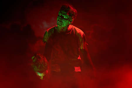 A terrible bloodthirsty zombie stands against the background of a red bloody sunset, surrounded by an ominous red fog. The Apocalypse. Halloween, horror movie.の写真素材