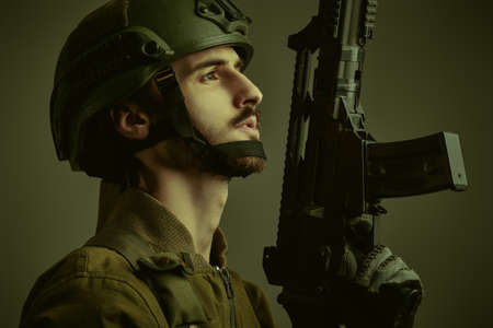 Sideview shot of a brave Army soldier in Protective Combat Uniform holding Special Operations Forces Combat Assault Rifle. Khaki background. War and military concept.の写真素材
