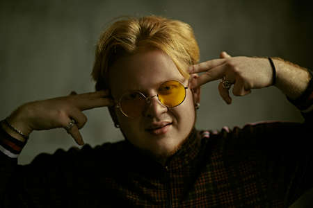 A modern guy with red hair and short beard wearing a casual sports suit and stylish glasses performs a street dance on a dark grunge background. Hip-hop culture. Rapper guy portrait.の写真素材