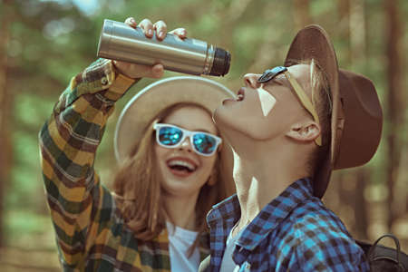 The guy and the girl drink tea from a thermos and have fun during a halt. Summer tourism, hiking. Vacation. Tourist equipment.の写真素材