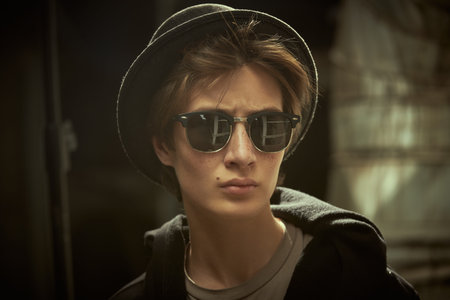 A modern teenage boy in a black hoodie and sunglasses stands on a city street. Modern young...