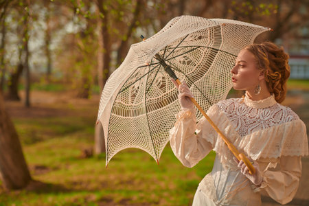 Vintage portrait of a beautiful aristocratic girl in a white lace dress with an umbrella walking...