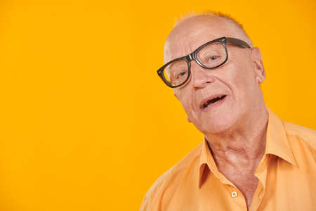 Happy senior man in casual wear and glasses smiles on a yellow studio background. Elderly people, healthy lifestyle. Copy space.の写真素材