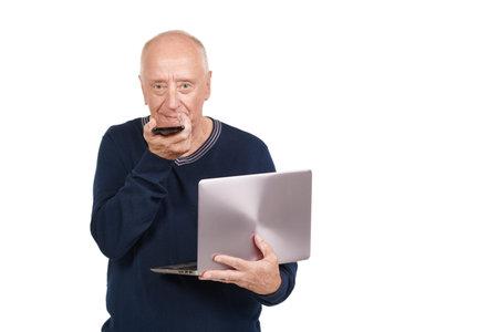 Pensioners and modern technologies. A senior man talks on the phone and holds a laptop in his hand....