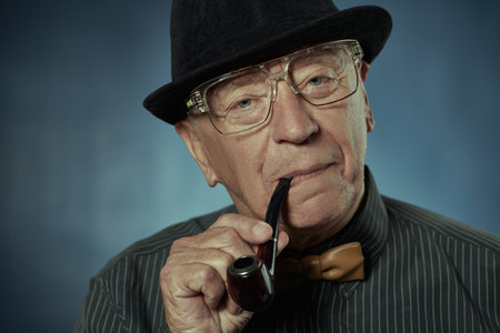 An old well-dressed gentleman smoking a pipe. Studio portrait on a dark blue background.