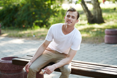 Joyful, smiling guy rests on the bench in the park on a nice summer day. Happy people, positive emotions, lifestyle.の写真素材