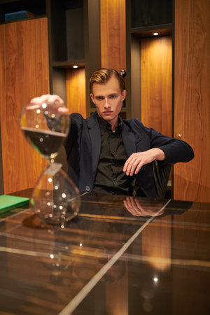A serious young businessman is sitting at his desk in his respectable office, deep in thought. There...
