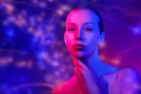 Female health and beauty. Art portrait of a beautiful tender girl with light natural makeup in mixed blue and crimson lighting. Studio portrait.  Copy space.の写真素材