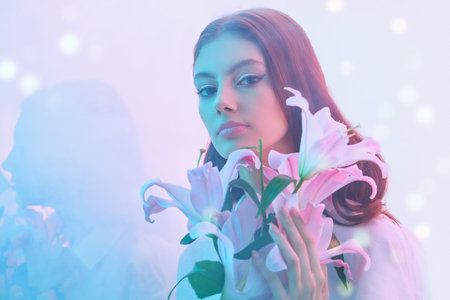 Beauty concept. Portrait of a beautiful brown-haired girl with delicate lily flowers on a gentle pink background with light haze and shining lights. Make-up and cosmetics. Perfumery.の写真素材